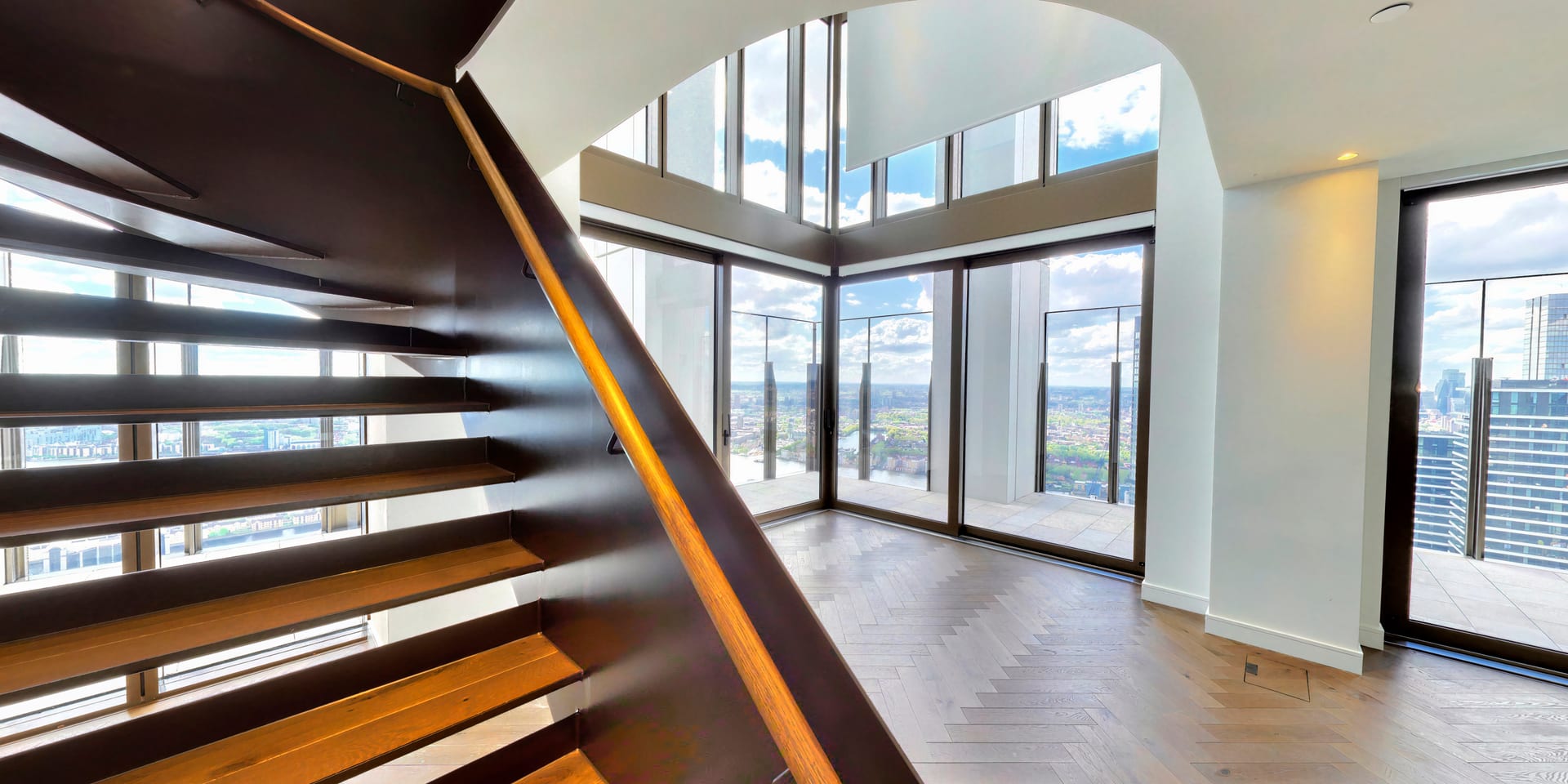 Terrace with curved glass balustrade framing a complete panorama of the Canary Wharf skyline